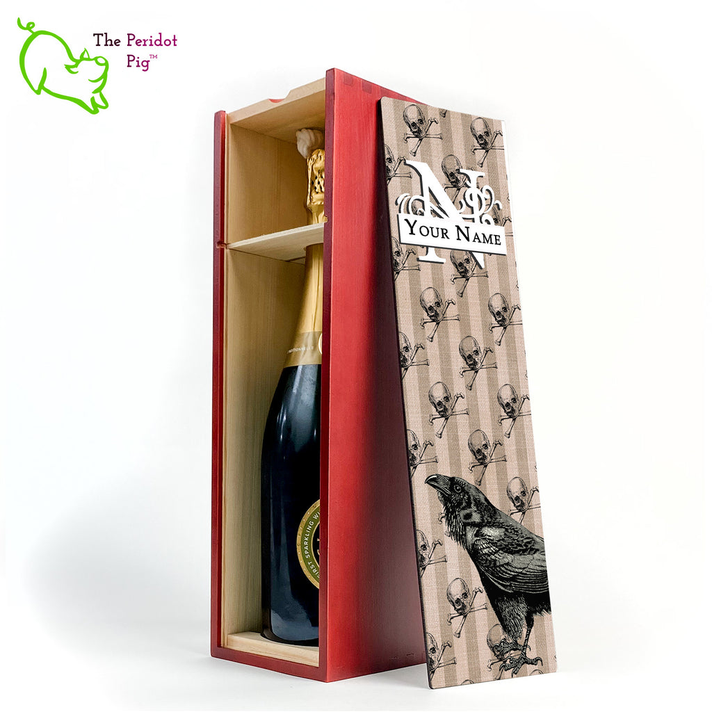 The front panel is decorated in a glossy, detailed print with a monogram and space for a customized name. This model has a striped linen background with skulls and crossbones overlaid. In the foreground is a large black raven. Front view in cherry showing the interior with a sample bottle of wine.