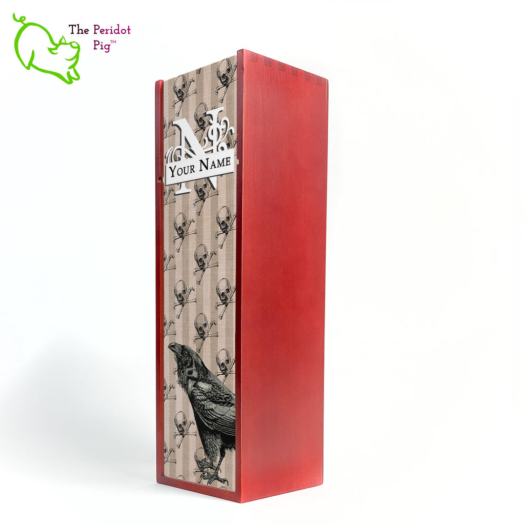 The front panel is decorated in a glossy, detailed print with a monogram and space for a customized name. This model has a striped linen background with skulls and crossbones overlaid. In the foreground is a large black raven. Front view in cherry.