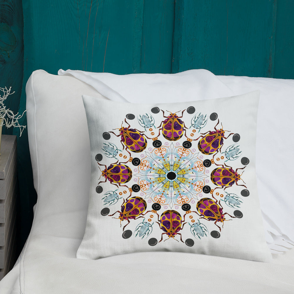 A colorful mandala of beetles graces this white pillow. The larger beetle has shades of violet surrounded by gold. The smaller beetle is in a delicate shade of blue. Printed on a bright, white casing these bugs really pop! Shown in size 18"x18" on a bed.